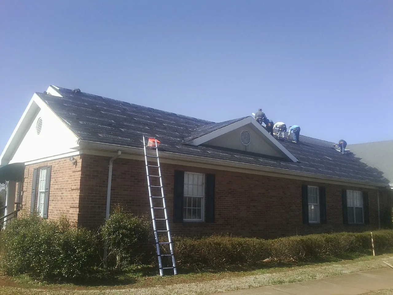 Crew tearing shingles off a brick ranch roof with a ladder set — Metal Roof Repair work by our crew in Camp Sherman