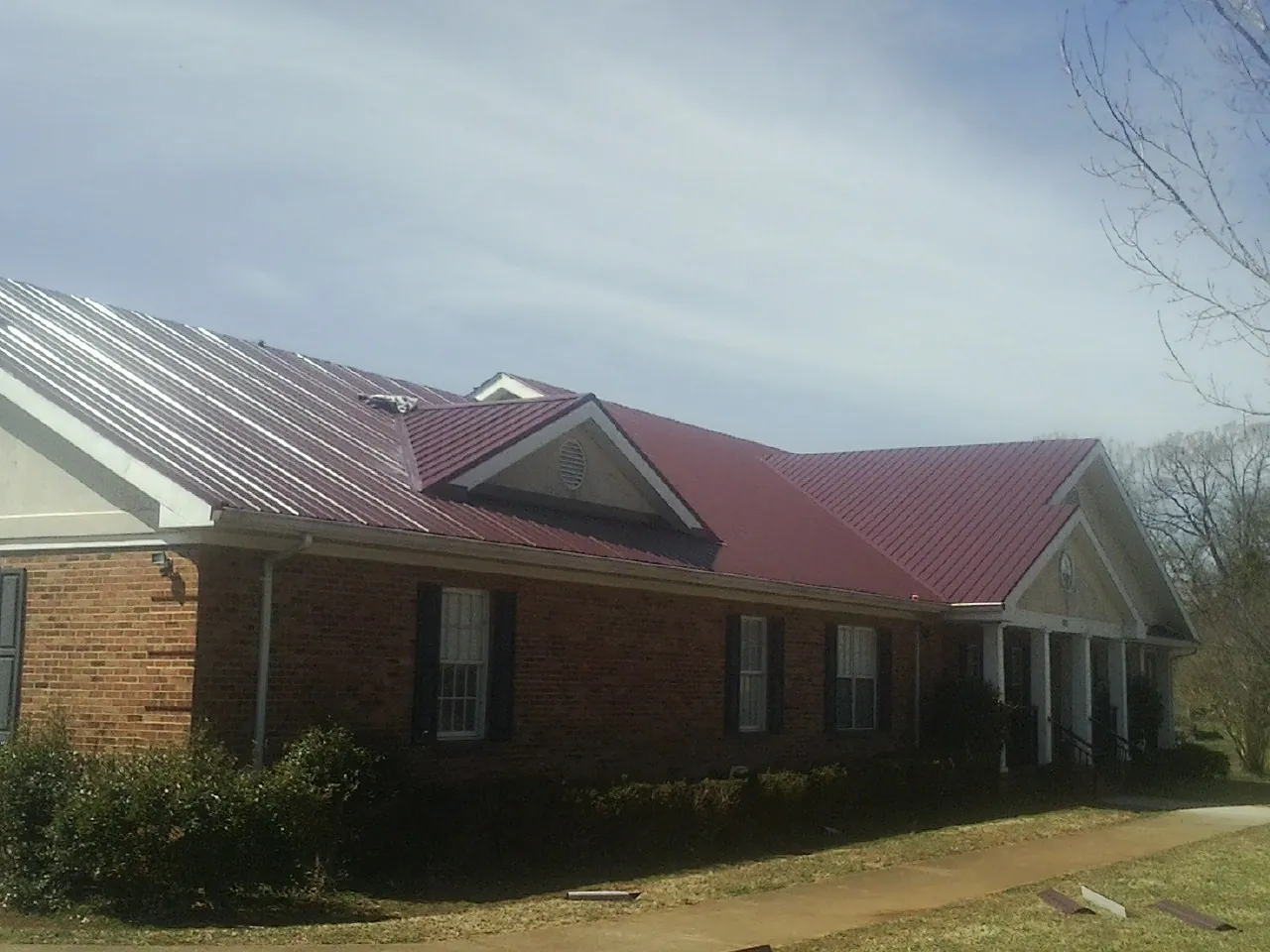 Red metal roof with gabled entries on a long brick building, from a Hail Damage Roof Repair job in Camp Sherman