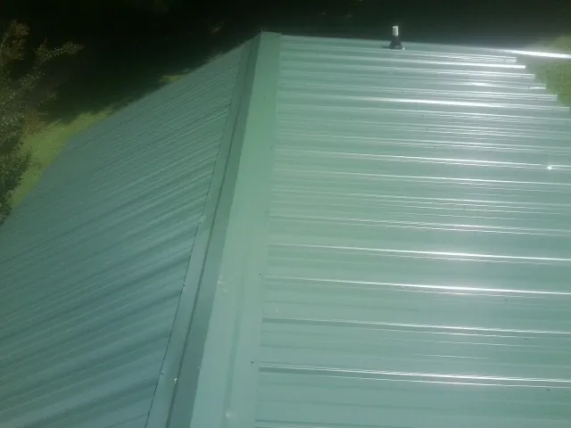 New green metal panels meeting at the ridge of a roof — Flat Roof Repair work by our crew in Camp Sherman