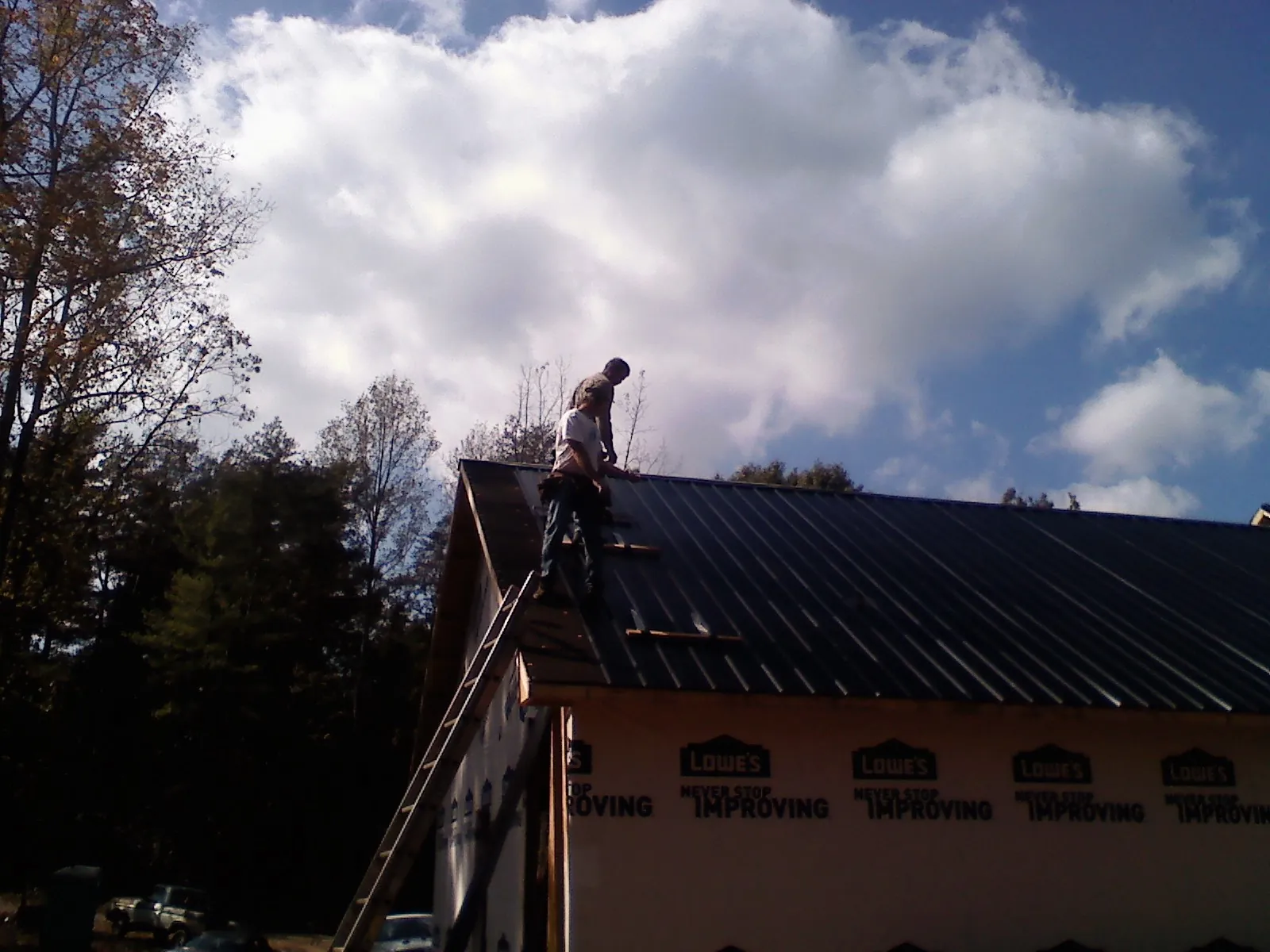 Roofer fastening dark metal panels high against a cloudy sky, from a Roof Inspection job in Camp Sherman