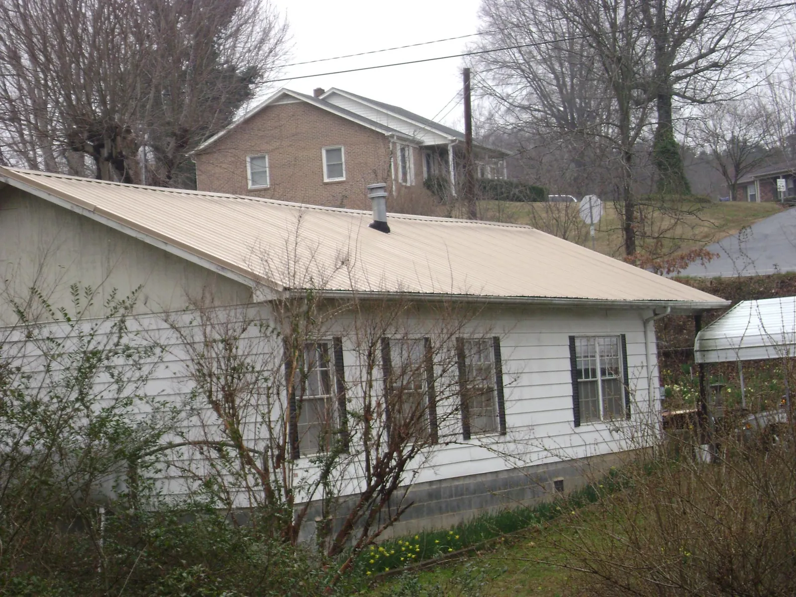 Tan metal roof on a white sided house set into a hillside — Commercial Roofing by Roofing Brothers in Camp Sherman