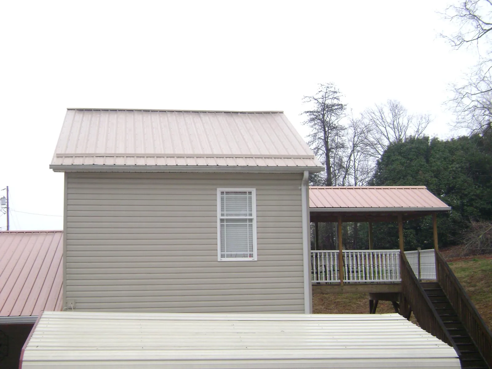 Tan metal roofs on a two story addition and attached porch, from a Roof Replacement job in Camp Sherman